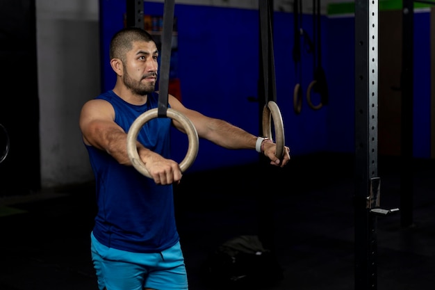 Retrato de um atleta em pé apoiado em anéis de ginástica em um local de treinamento