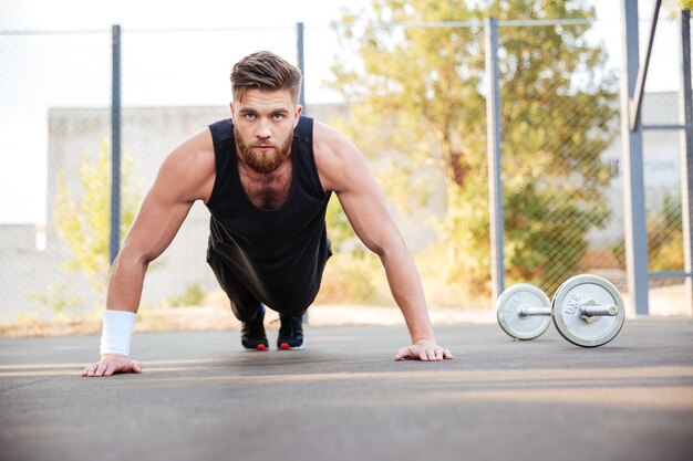 Retrato de um atleta jovem barbudo concentrado fazendo exercícios de prancha ao ar livre