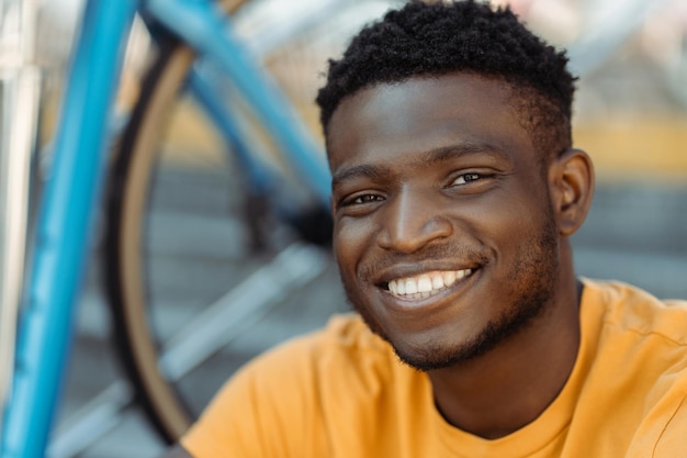 Retrato de um atrativo e sorridente ciclista nigeriano vestindo uma camiseta laranja.