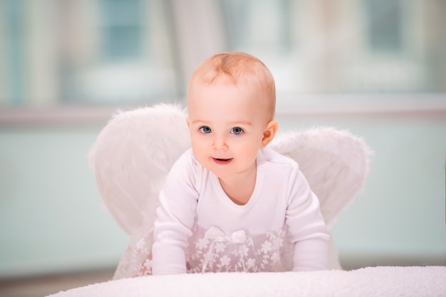 Retrato de um bebê alegre e travesso com asas de anjo branco rastejando em direção ao observador