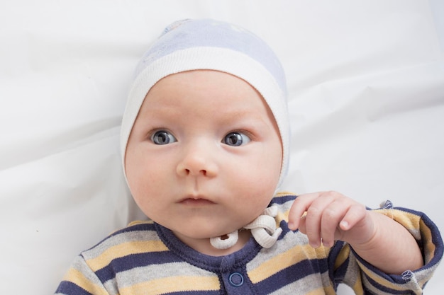 Retrato de um bebê com uma cara de expressão engraçada no lençol branco. Camada plana, vista superior.