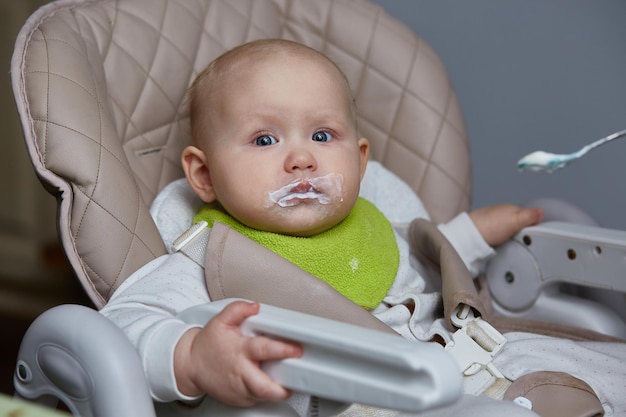 Retrato de um bebê comendo em uma cadeira alta pela primeira vez com uma colher.