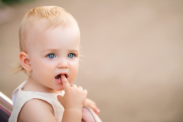 Retrato de um bebê de olhos azuis chupando um dedo na boca, dois primeiros dentes são visíveis.