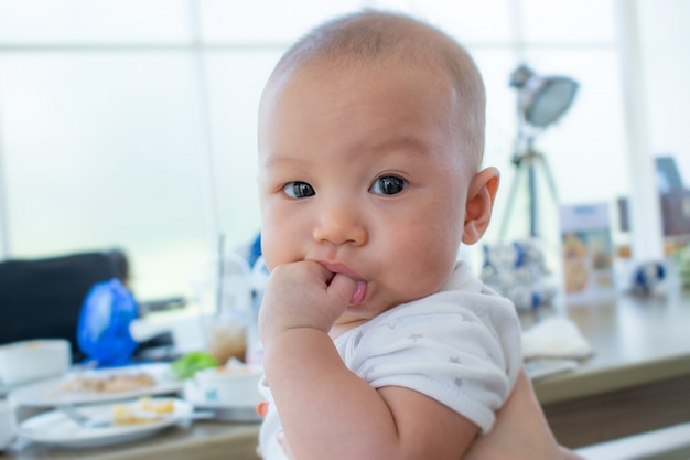 Foto retrato de um bebê de sorriso adorável que morde para possuir os dedos que põem seu punho em sua boca.