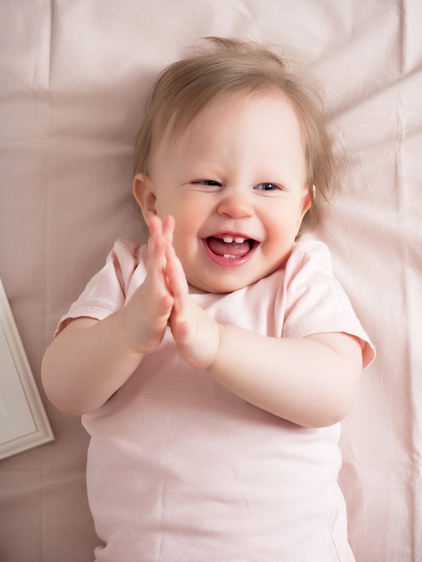 Retrato de um bebê feliz e sorridente, com uma expressão engraçada no rosto. uma linda garotinha de olhos azuis sorri alegremente, os primeiros dentes são visíveis.