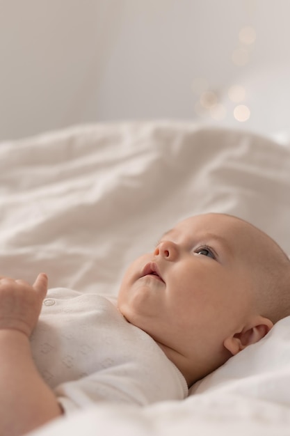 Foto retrato de um bebê fofo em uma roupa branca em uma cama em casa com lençóis brancos. bebê recém-nascido em casa