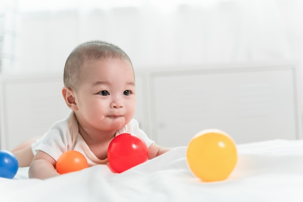 Retrato de um bebê rastejando na cama no quarto dela e jogando bola brinquedo