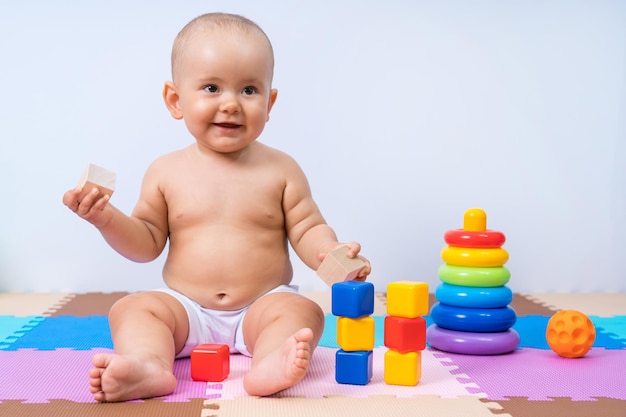 Retrato de um bebê recém-nascido sentado de 8 a 12 meses com cubos de madeira nas mãos. Criança feliz na sala de jogos