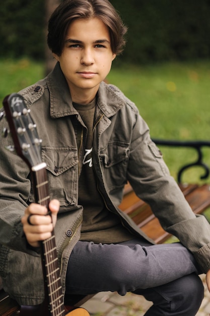 Retrato de um belo adolescente tocando guitarra ao ar livre, usando um violão clássico masculino sozinho, fazendo