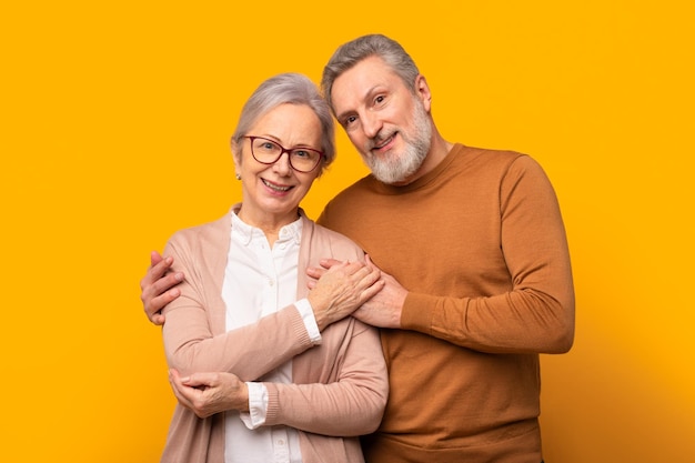 Retrato de um belo casal idoso abraçando-se com amor estúdio amarelo