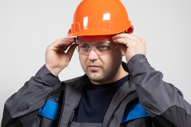 Retrato de um belo construtor de trabalhadores com capacete de macacão e óculos em um fundo branco