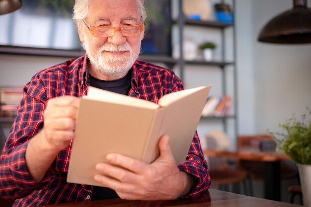 Retrato de um belo homem barbudo sênior sentado na mesa do café lendo livro aproveitando o tempo livre