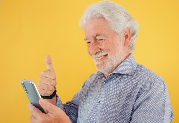Retrato de um belo homem barbudo sorridente isolado em fundo amarelo com o polegar para cima enquanto usa o telefone no bate-papo por vídeo