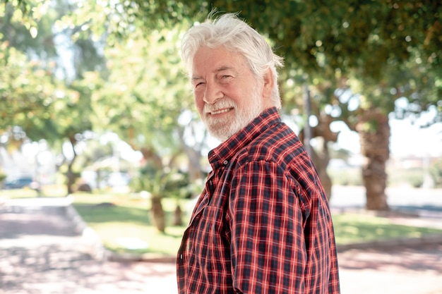 Retrato de um belo homem de cabelos brancos sênior caminhando no parque da cidade olhando para a câmera sorrindo