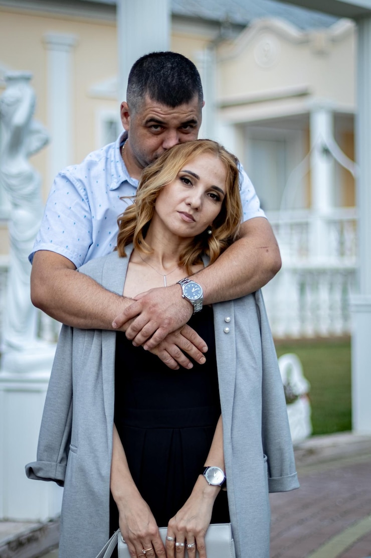 Foto retrato de um belo jovem casal feliz caucasiano de pé em um abraço em um pátio com colunas brancas e olhando para a câmera em close-up vista lateral