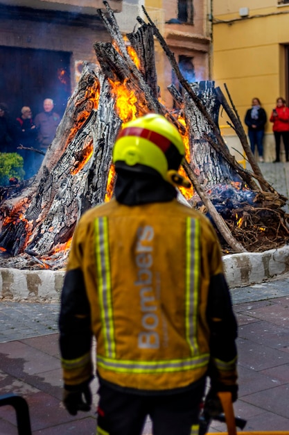 Retrato de um bombeiro usando aparições de bombeiro e capacete chamas ao fundo com fumaça e luz azul