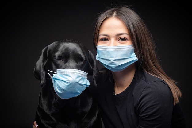 Retrato de um cão Labrador Retriever em uma máscara médica protetora com uma dona do sexo feminino