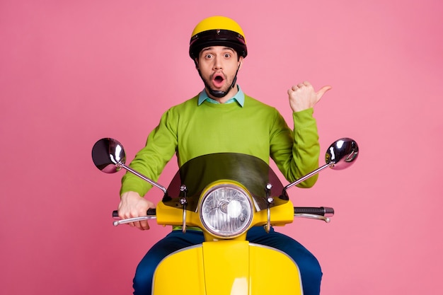 Retrato de um cara alegre surpreso andando de motocicleta indica dedo