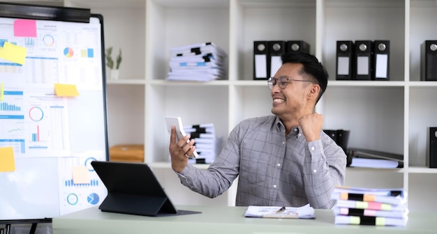 Retrato de um cara asiático animado alegre usando pc sentado na mesa olhando para a tela do laptop levantando as mãos com excitação homem entusiasmado em êxtase agitando os punhos comemorando o sucesso