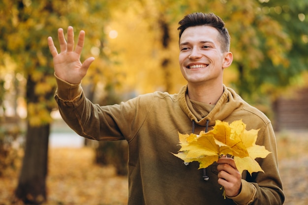 Foto retrato de um cara bonito e feliz sorrindo e cumprimentando no parque outono