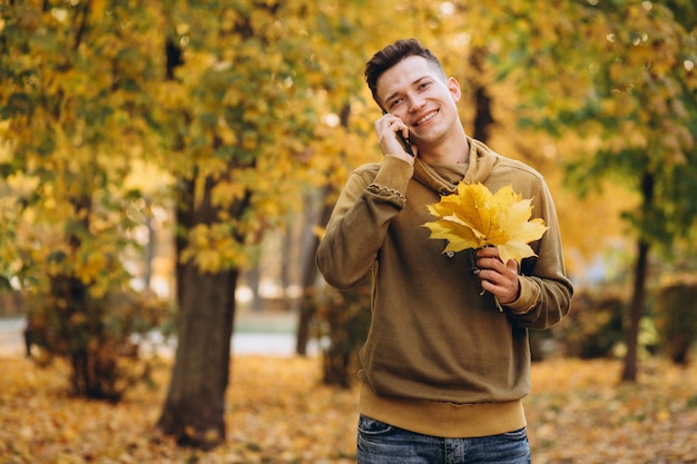 Retrato de um cara bonito e feliz sorrindo e falando ao telefone no parque outono