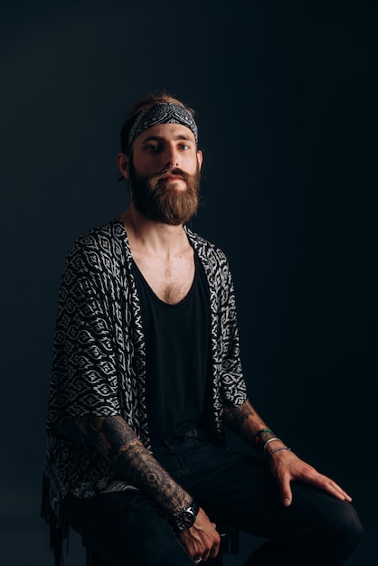 Foto retrato de um cara com barba e tatuagens em um hipster de fundo escuro