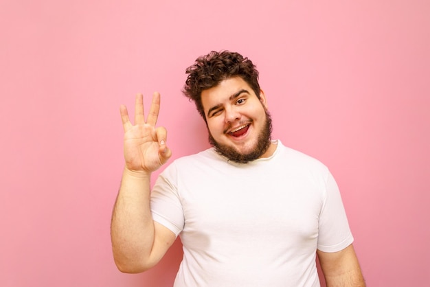 Retrato de um cara feliz com cabelo encaracolado e excesso de peso em um fundo rosa