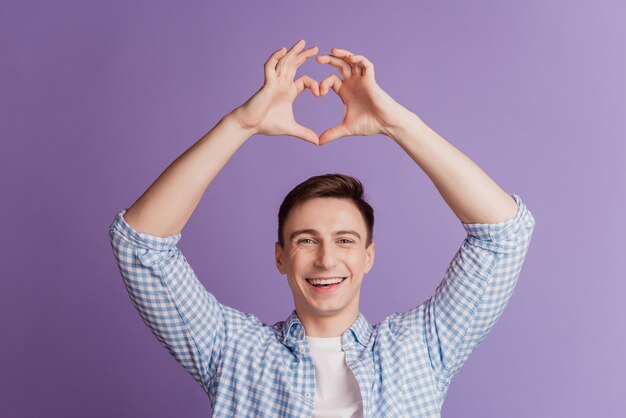 Retrato de um cara romântico sonhador mostra o símbolo do coração de amor em fundo roxo