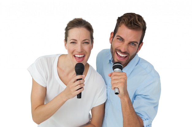 Retrato de um casal alegre cantando em microfones