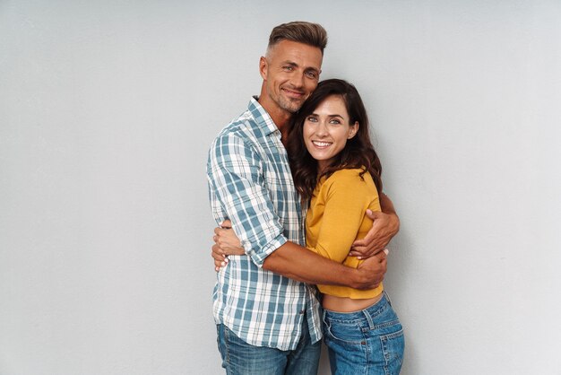 Retrato de um casal amoroso adulto alegre positivo abraçando isolado sobre uma parede cinza.