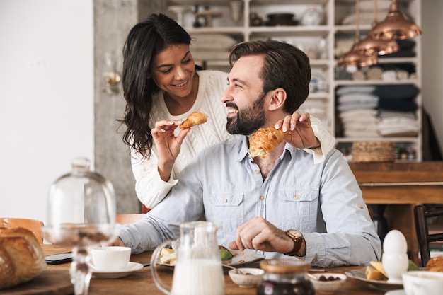 Retrato de um casal apaixonado, homem e mulher, comendo juntos à mesa, enquanto tomam café da manhã na cozinha de casa