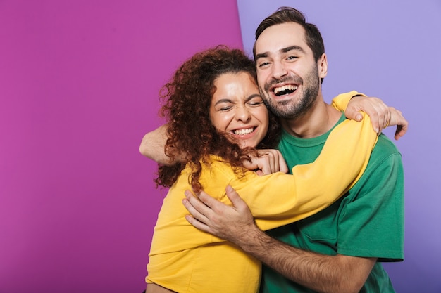 Foto retrato de um casal caucasiano animado, homem e mulher com roupas coloridas, regozijando-se e abraçando-se juntos e isolados