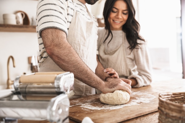 Retrato de um casal caucasiano, homem e mulher de 30 anos, usando aventais, misturando a massa enquanto cozinham na cozinha de casa