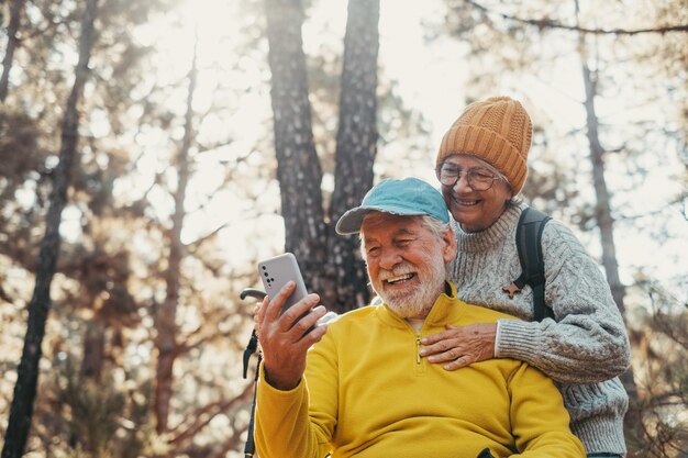 Retrato de um casal de idosos bonitos usando o telefone juntos na floresta com árvores