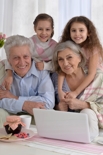 Foto retrato de um casal de idosos feliz com netos e laptop em casa