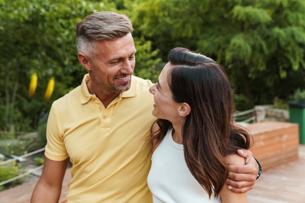 Retrato de um casal de meia-idade sorridente, homem e mulher, olhando um para o outro e se abraçando enquanto caminhava no parque de verão