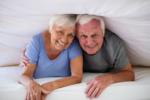 Retrato de um casal feliz de idosos embaixo do cobertor, na cama do quarto