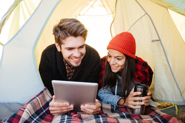 Retrato de um casal feliz deitado em uma barraca e usando um computador tablet juntos