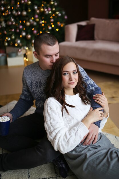 Retrato de um casal feliz e apaixonado perto de uma árvore de Natal e bokeh em uma casa aconchegante