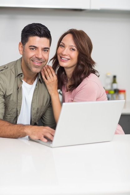 Retrato de um casal feliz usando laptop na cozinha