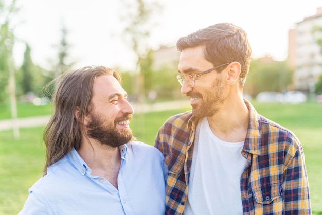 Retrato de um casal gay alegre olhando um ao outro no parque em um dia ensolarado