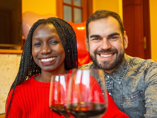 retrato de um casal inter-racial olhando um para o outro rindo com copos de vinho tinto desfrutando.