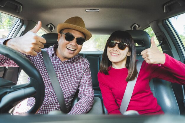 Retrato de um casal mostrando os polegares para cima enquanto está sentado no carro