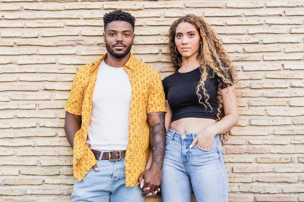 Retrato de um casal multirracial feliz e apaixonado, sorrindo juntos em um fundo de tijolos.