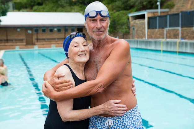 Retrato de um casal sorridente de idosos se abraçando à beira da piscina