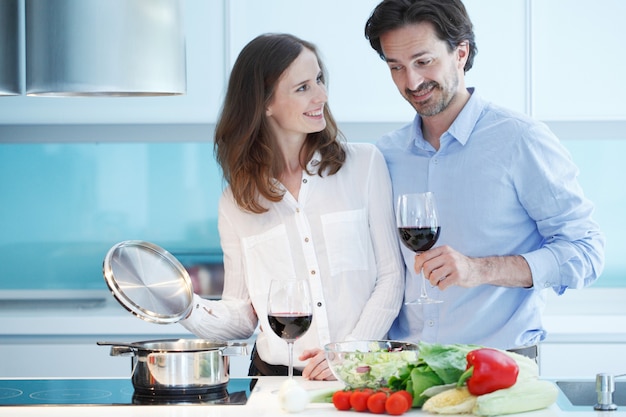 Retrato de um casal tomando uma taça de vinho tinto enquanto cozinha o jantar