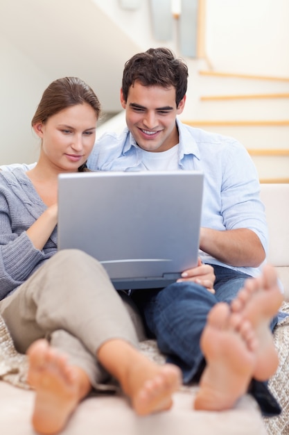 Retrato de um casal usando um laptop enquanto estava deitado em um sofá