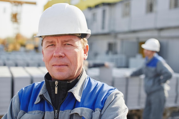 Retrato de um construtor de macacão e capacete no fundo de um grupo de pessoas ao redor de um carrinho com um tijolo