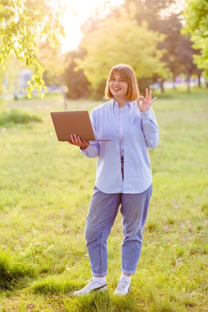 Retrato de um corretor de agente de garota alegre e atraente usando laptop se divertindo no parque verde