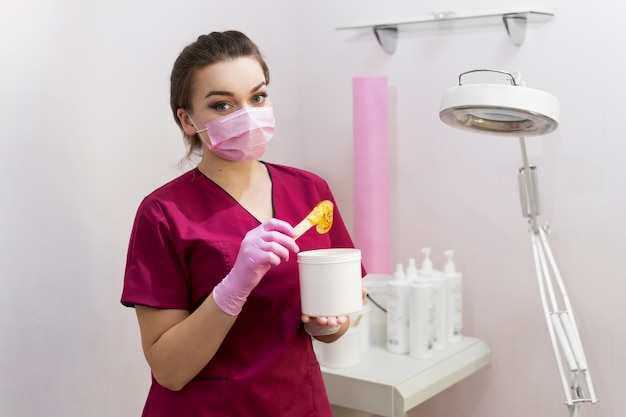 Retrato de um cosmetologista com pasta de açúcar para depilação. shugaring. pasta de açúcar fora do recipiente com uma espátula. pasta de açúcar para adoçar. sugaring no salão de beleza